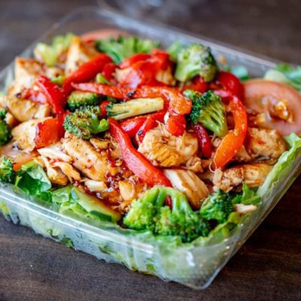 Chicken and broccoli salad with red peppers and tomatoes in a clear plastic container.
