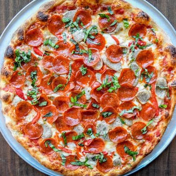 Buccieri's Pizzeria pepperoni and sausage pizza with fresh basil on a metal tray.